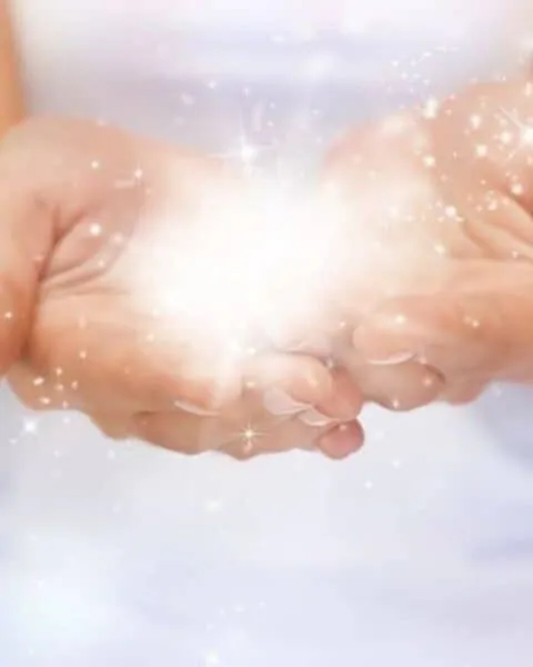 A woman cupping her hands and holding a burst of light.