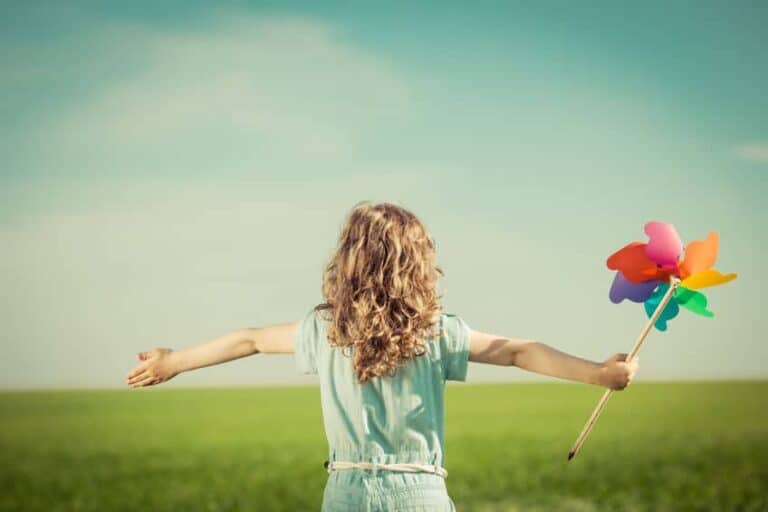 A small child with her arms stretched out in the middle of a grassy field.