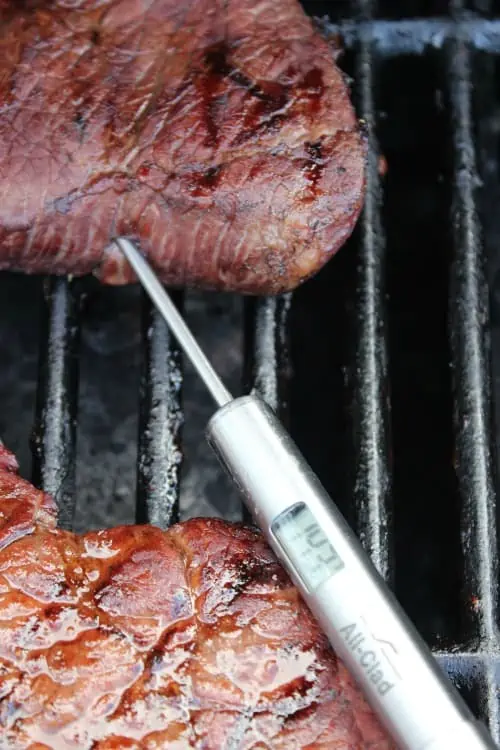 A close up of a slice of beef on a grill with a temperature gauge. 