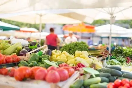 farmers\' food market stall with variety of organic vegetable. vendor serving and chatting with customers.