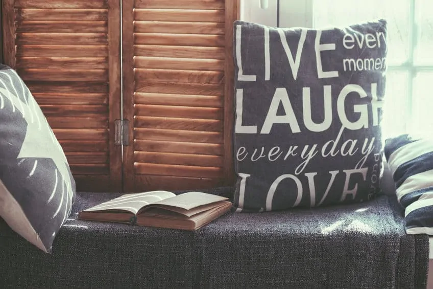 warm and cozy window seat with cushions and a opened book, light through vintage shutters, rustic style home decor.