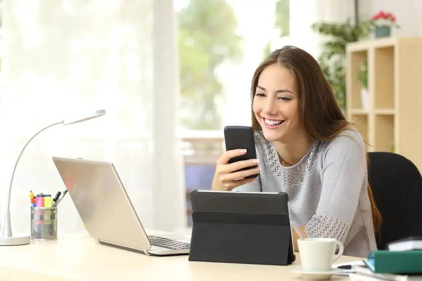 happy woman working using multiple devices on a desk at home