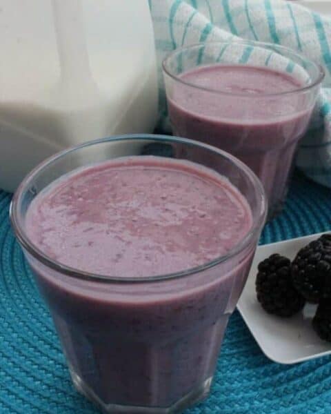 Two cups full of blackberry smoothie with fresh blackberries.