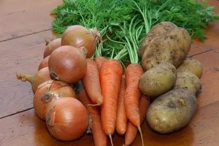 a selection of root vegetables onions, carrots and potatoes on a wooden kitchen table