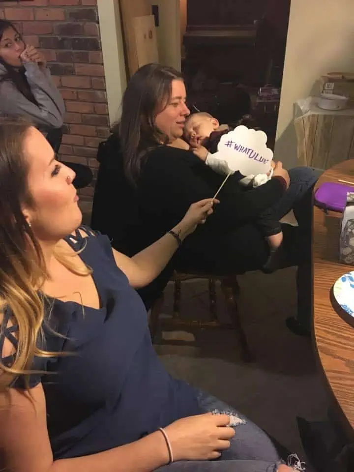 A woman sitting at a table holding a sleeping newborn.