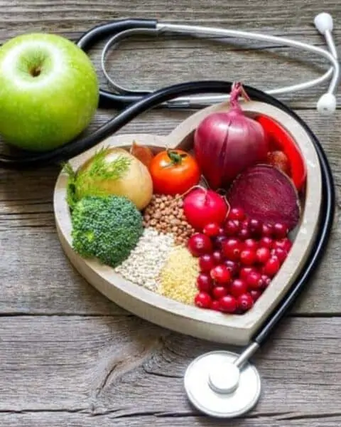 A heart shaped bowl with healthy fruits, vegetables, and grains on the inside of the bowl.
