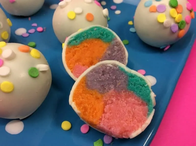 Rainbow cake balls dipped in frosting and sprinkles.