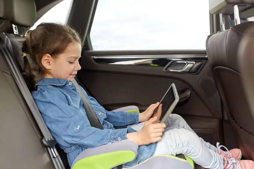 a young girl is reading her tablet while riding in the car.