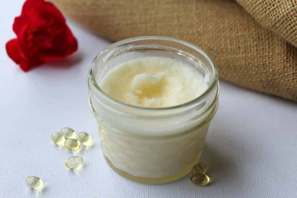 A jar of homemade eye cream sitting on a table with vitamin E capsules. 