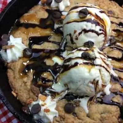 Assortment of camping desserts including campfire apple crisp, campfire cobbler, and campfire brownies prepared in cast iron skillets and foil packets.