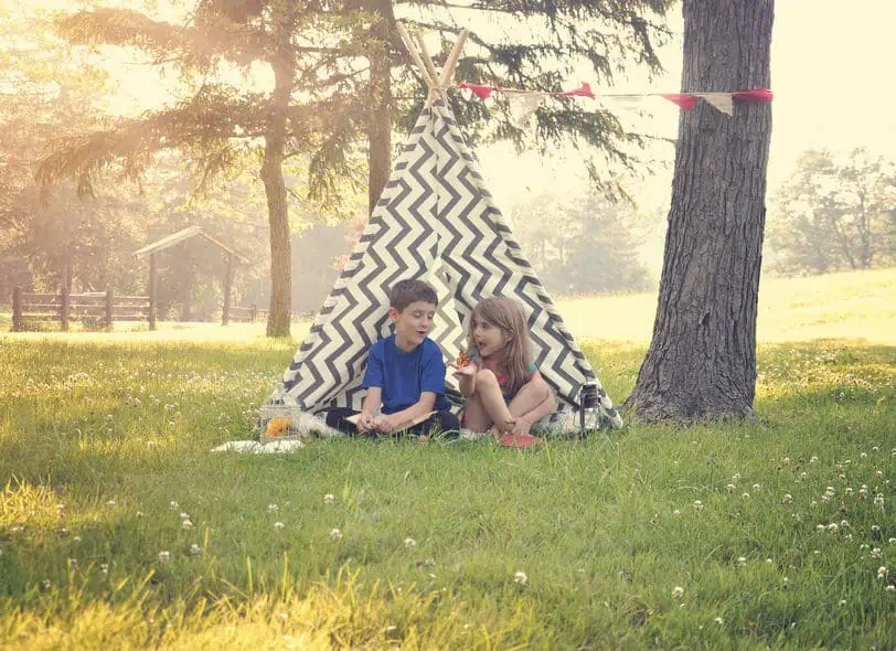 A couple of kids playing outside in a homemade tee pee and enjoying the cool summer weather.