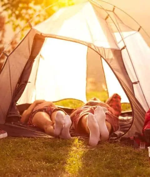 A couple laying down inside a tent with the flaps open. How to plan an awesome staycation for your family.
