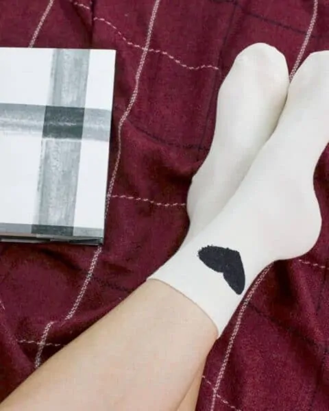 White socks with a black heart next to a journal and cup of coffee.