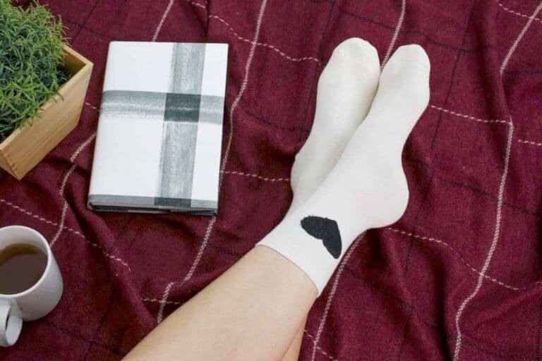 White socks with a black heart next to a journal and cup of coffee.