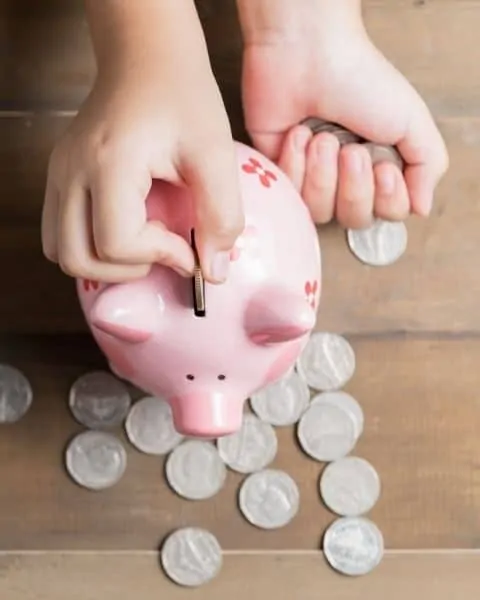 kid putting change into a pink piggy bank