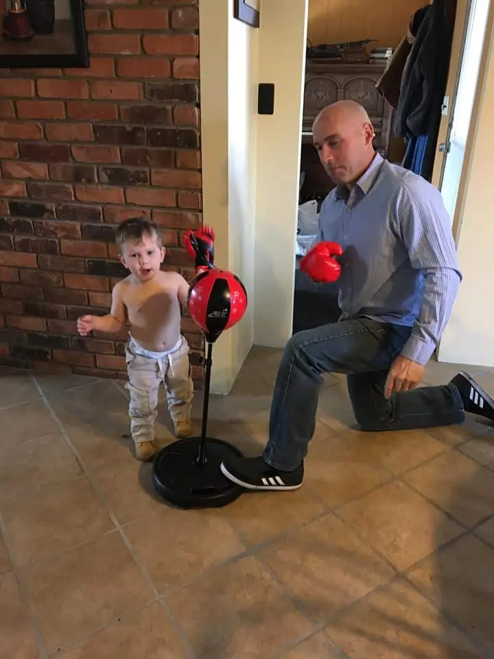 A man with his grandson boxing and hitting a punching bag.