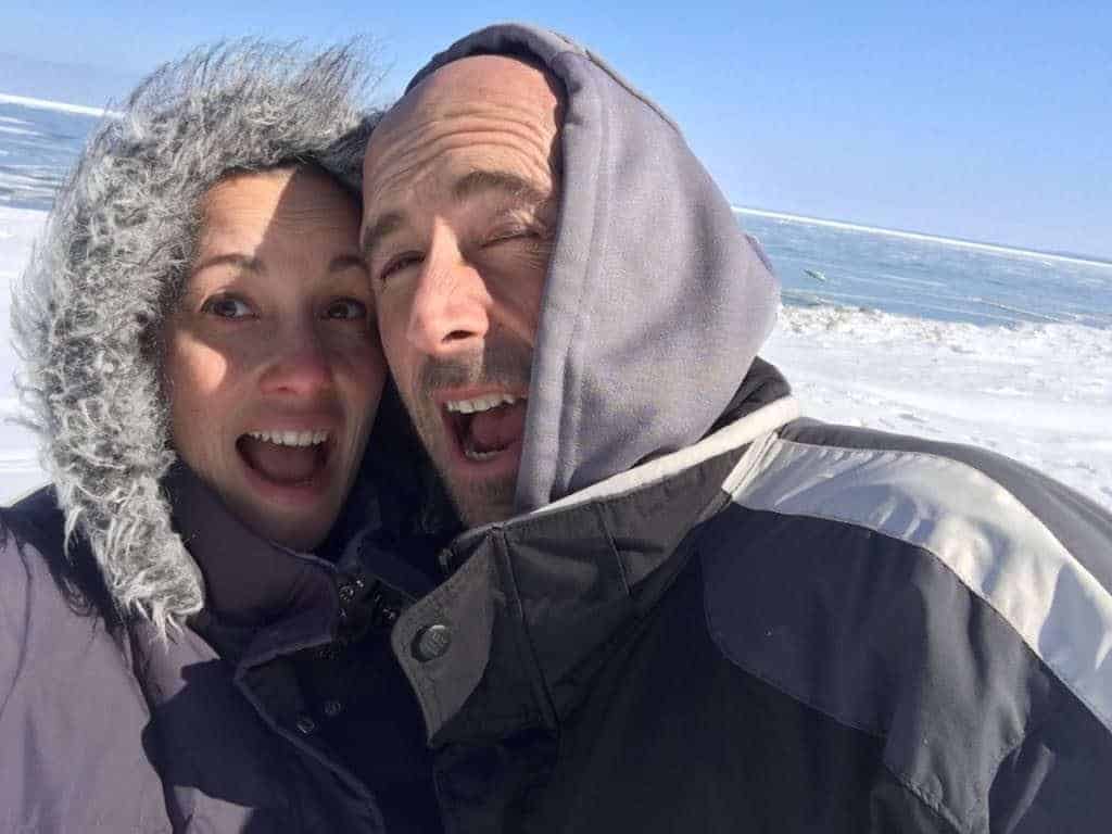 A couple posing and smiling on the beach in the middle of winter.
