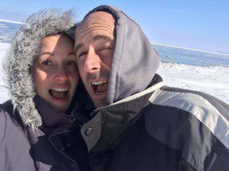 A couple of people posing for the camera, smiling in front of a beach.