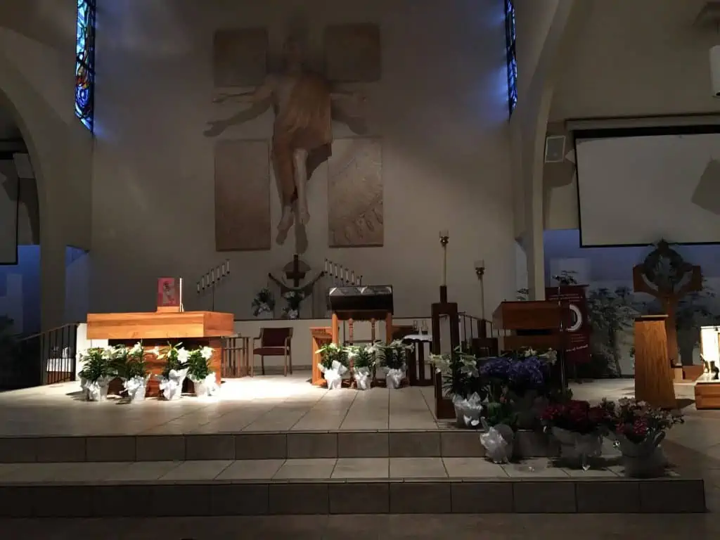 Light falling on the baptismal font in front of a statue of Christ on the cross.
