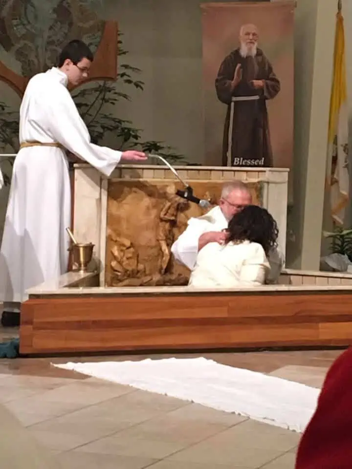 A man baptizing a woman in a font.