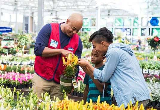 A Lowes employee standing in front of a flower helping a family of customers.