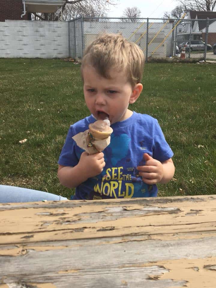 A little boy sitting at a picnic table eating ice cream.