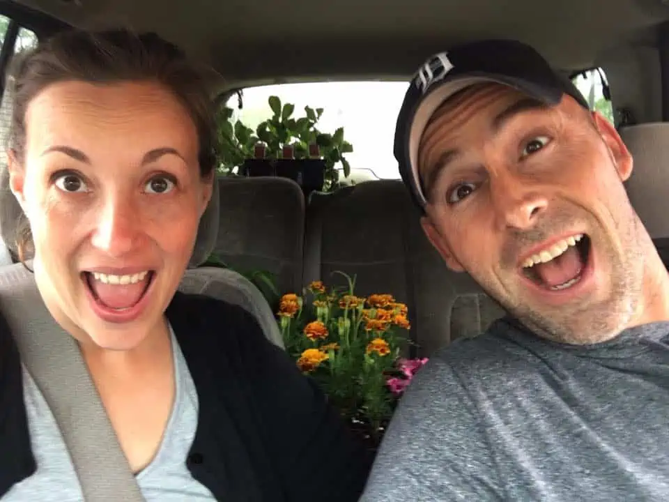 A man and a woman smiling for the camera with flowers in the back seat.