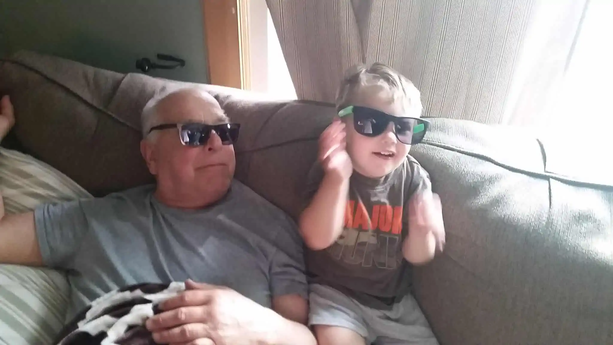 Grandson and great-grandfather wearing matching sunglasses and smiling together.
