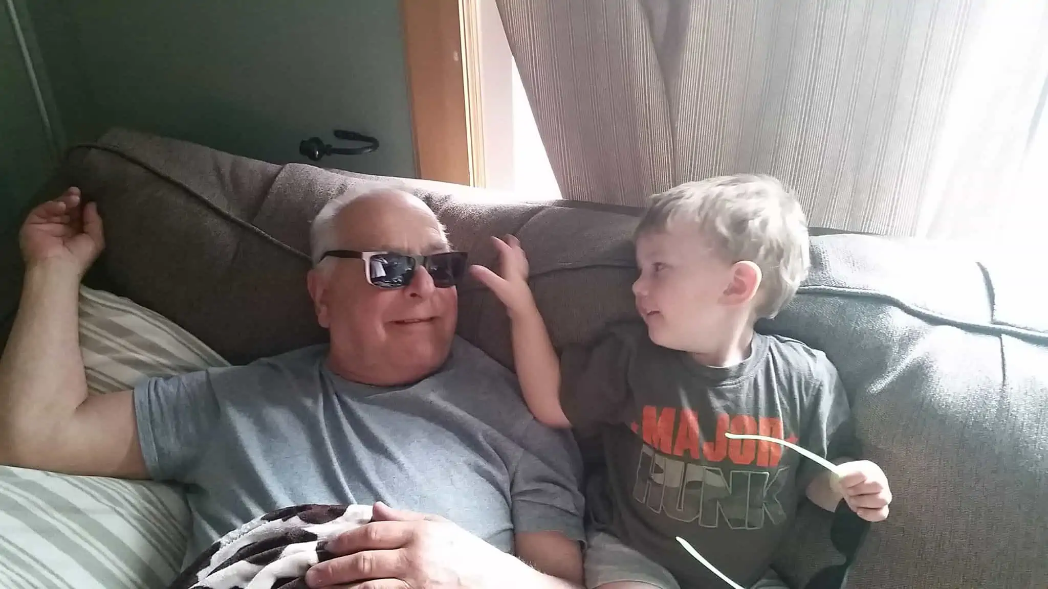 Grandpa sitting next to grandson. Both are smiling and having fun.