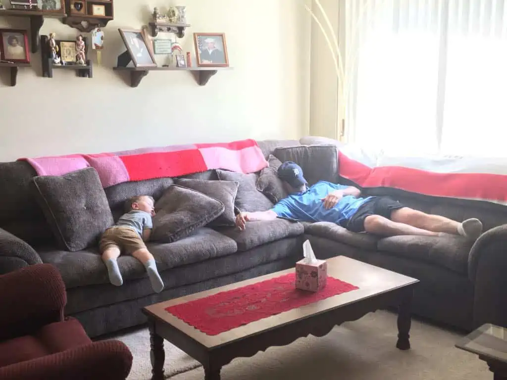 A grandfather and grandson napping on the couch. 