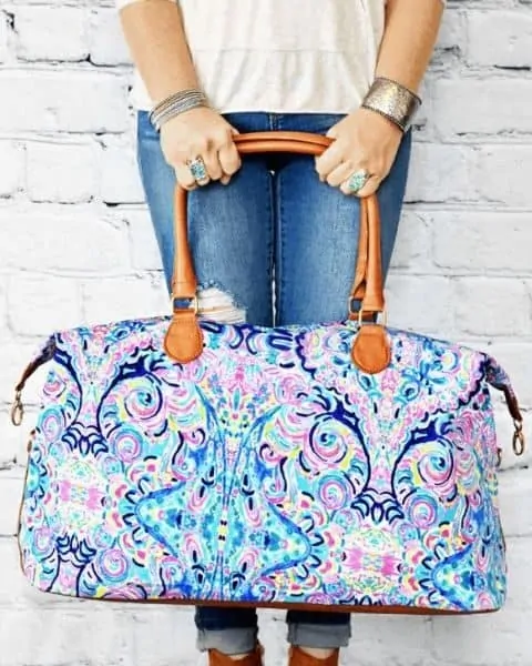woman holding a paisley weekender bag while standing against a white brick wall