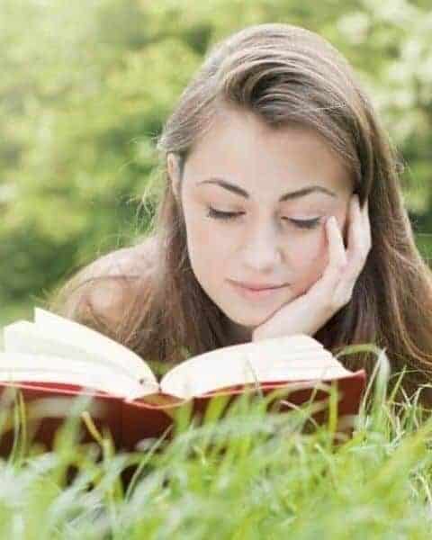 Young woman laying in the grass reading a book.