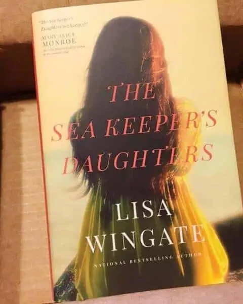 A book sitting on top of a table. The Sea Keeper's Daughters by Lisa Wingate.