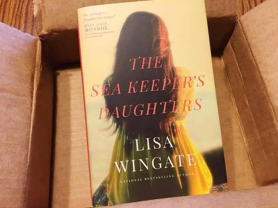 A book sitting on top of a table. The Sea Keeper\'s Daughters by Lisa Wingate.