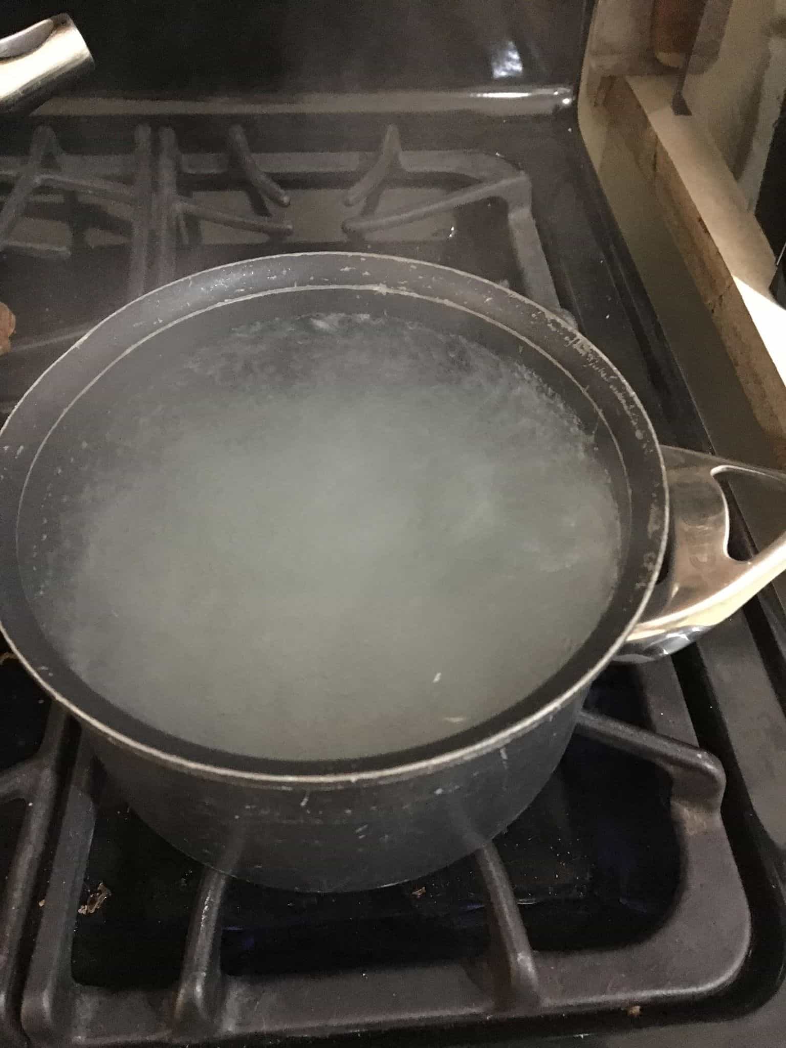 A close up of a metal pan on a stove, with Boiling water.