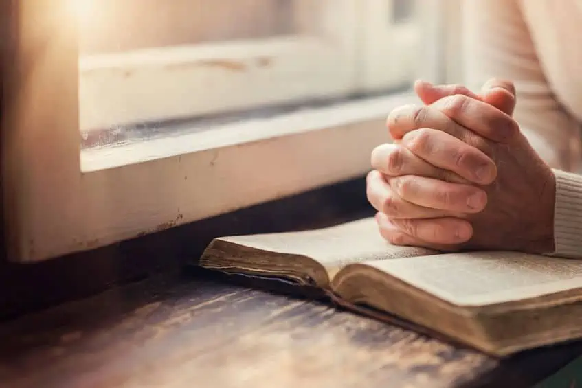 A woman folding her hands over her Bible in prayer.