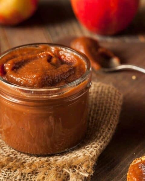 Jar of apple butter made from the crock pot surrounded by apples and bread slices.