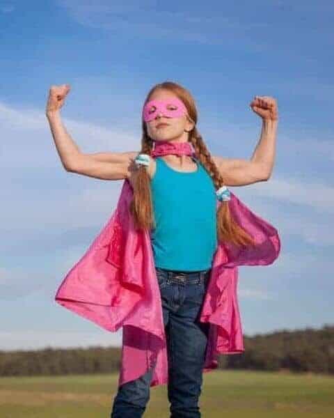 a girl with braids standing outside wearing a pink cape and flexing her bicep muscles