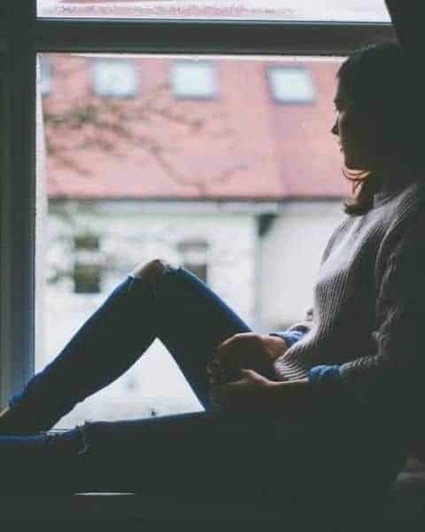 woman sitting beside a window and looking outside at a dreary day