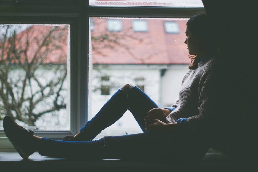 Woman sitting on the edge of the window, looking outside.