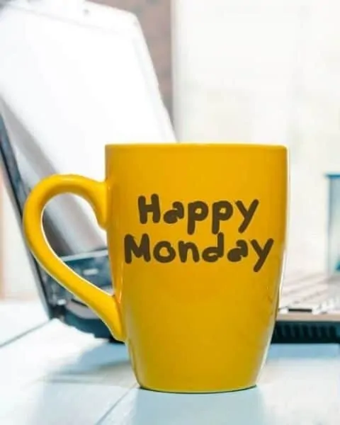 a yellow mug that says Happy Monday on it, in front of a laptop