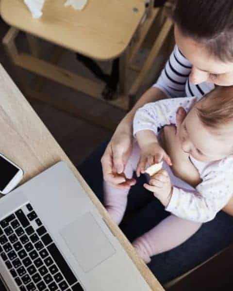 a mother sitting at her laptop with her baby in her lap
