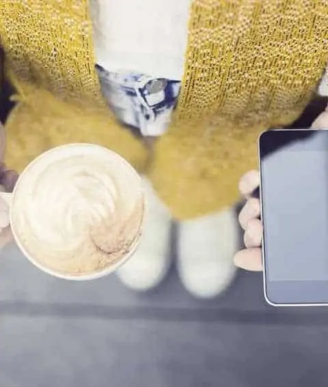 A woman drinking a cup of latte while being on her phone.