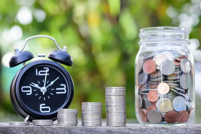 Alarm clock by a stack of coins and a jar full of money. How to save money by meal planning.