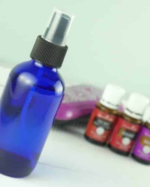 spray bottle in front of three bottles of essential oils and a hairbrush