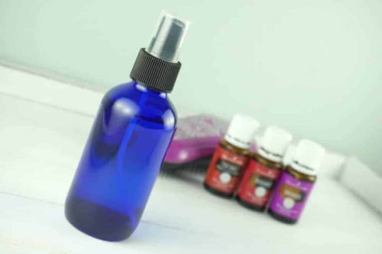 spray bottle in front of three bottles of essential oils and a hairbrush