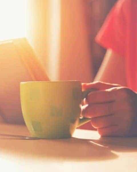 woman drinking coffee at a table while reading a book