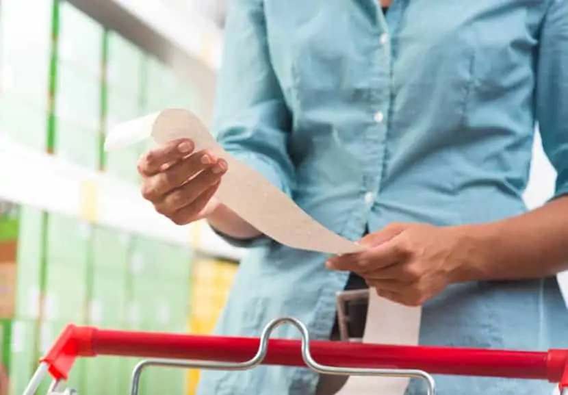 Woman looking over grocery receipt after buying groceries in order to save money.