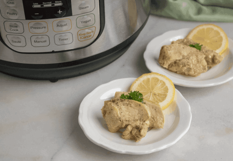 Two white plates with cooked chicken and lemon slices.