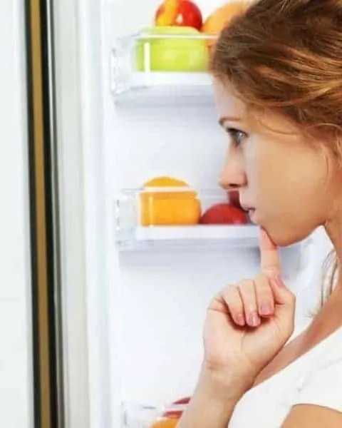 woman standing in front of an open fridge trying to decide what to make for dinner
